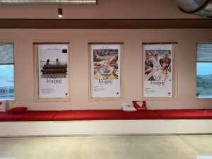 A wall with three posters advertising 'Oceania Voyages,' depicting cruise activities and destinations, above a red cushioned bench with branded pillows.