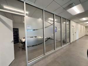 Office conference room with frosted glass walls featuring abstract designs, open white door, and visible text on a wall banner listing company values.