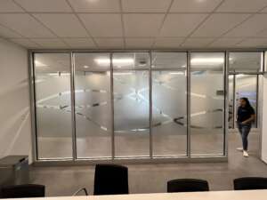 A person walks through a glass door in a modern office space, featuring frosted glass walls with abstract designs.