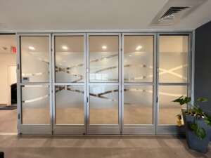 A modern glass partition with frosted designs in an office space. There is minimal decoration except for a potted plant in the right corner.