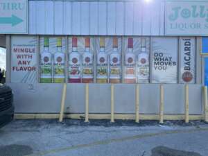 A storefront display showcasing various flavors of Bacardi rum bottles with promotional slogans, located beside a parking lot.