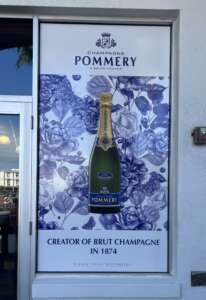 Advertising poster for Pommery champagne featuring a bottle of Brut champagne, blue floral graphics, and text stating "Creator of Brut Champagne in 1874" with "Please Drink Responsibly" at the bottom.