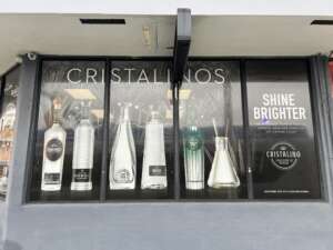 A storefront window display featuring various bottles of Cristalino tequila with text that reads "Cristalinos" and "Shine Brighter.