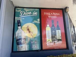 Advertisement in a storefront window showcasing "Deep Eddy Vodka" and "Stella Rosa Wines," with colorful graphics and images of the bottles.