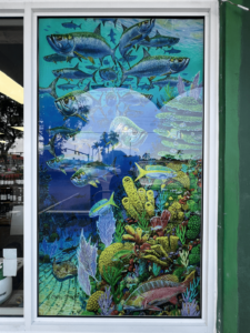 Detailed colorful mural depicting an underwater scene with various fish swimming over corals and sea plants, visible through a store window.